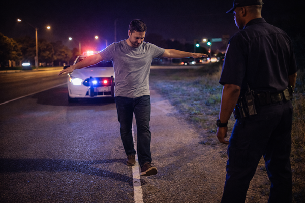 A police officer watches a driver perform a field sobriety test on the side of a road at night with patrol car lights flashing, illustrating the type of evidence captured by body camera footage in Texas DWI cases.
